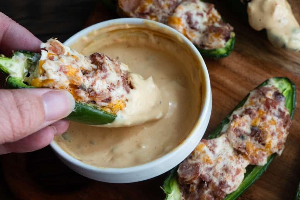bacon cheeseburger jalapeno poppers being dipped in sauce