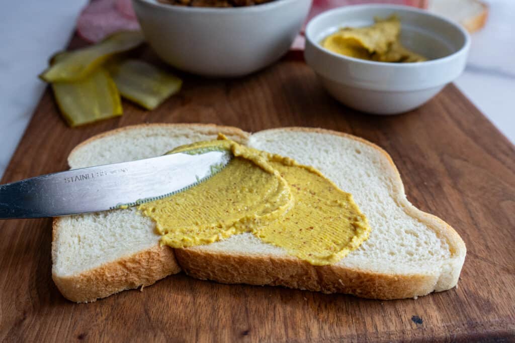 Spreading yellow mustard on bread for the smoked cuban sandwich recipe