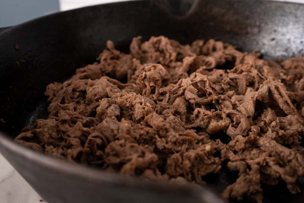 Shaved beef cooked in a skillet.