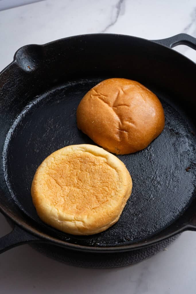 Brioche buns being toasted in a skillet.