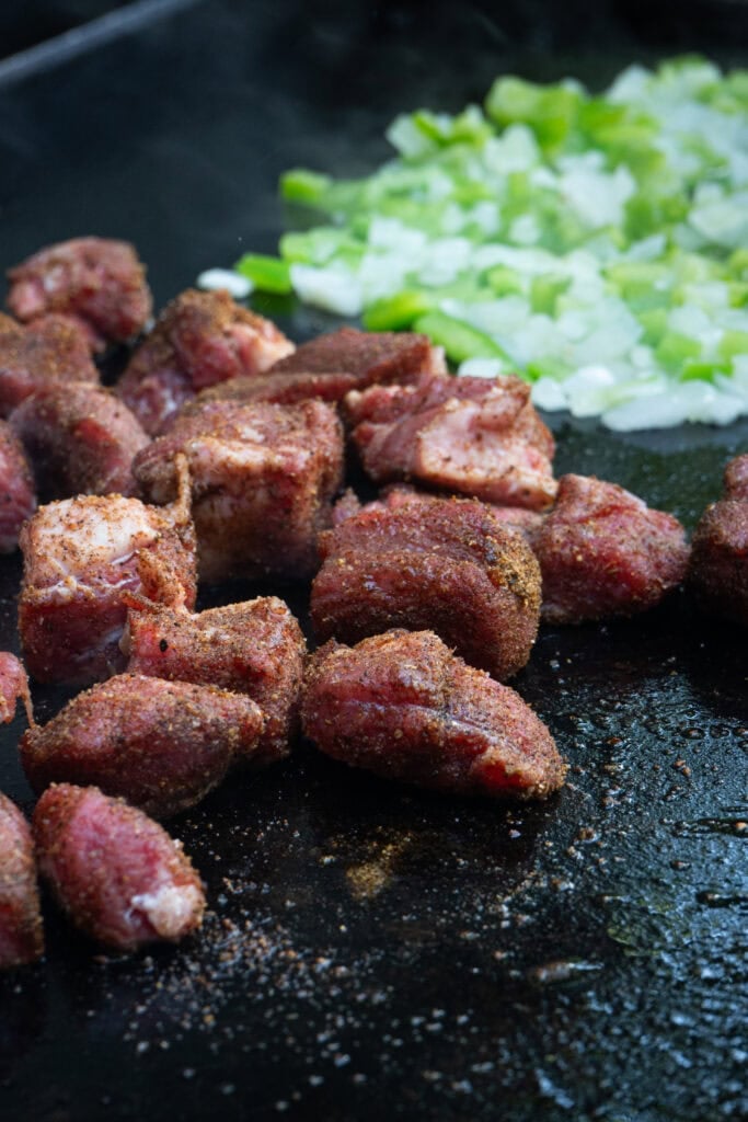 Steak, peppers and onions cooking on a griddle.