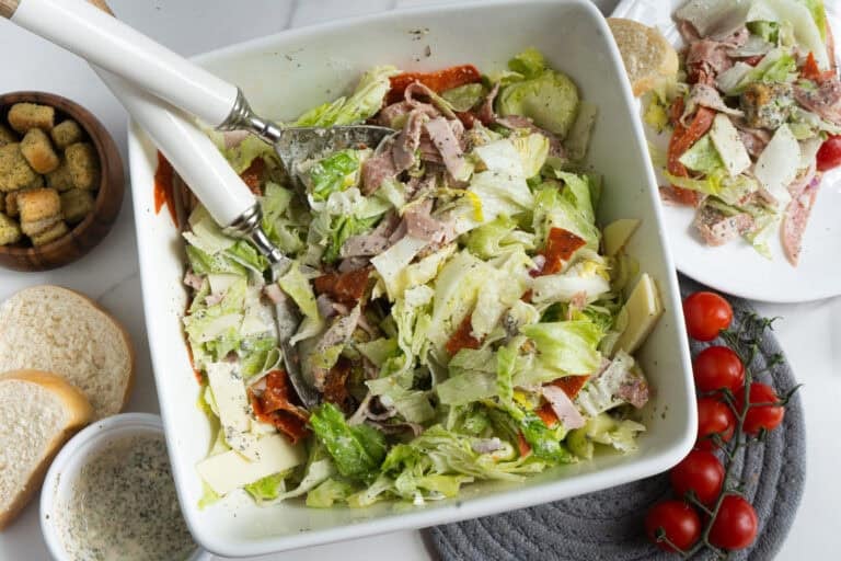 A salad with meat, lettuce and tomatoes in a white bowl.