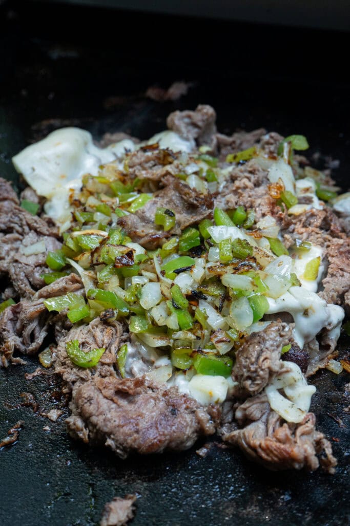 Steak onions peppers cooking on a griddle.