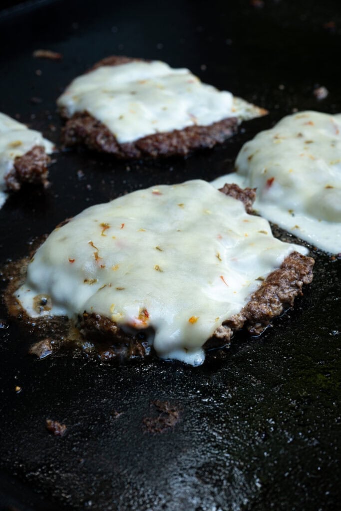 Burgers on the griddle with pepper jack cheese.