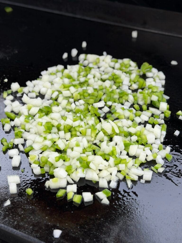 Green bell pepper and onion cooking on a griddle.