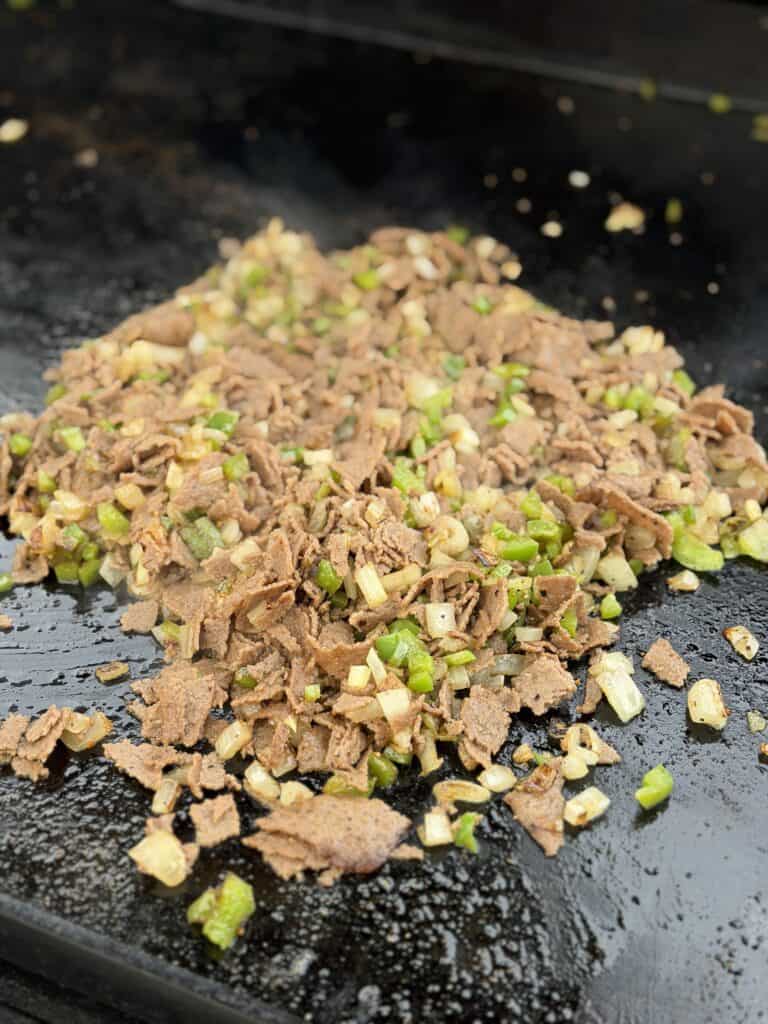 Steak, pepper and onion mixture on a griddle.