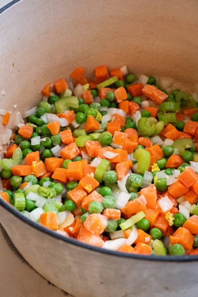 carrots, onions and peas cooking in a dutch oven.