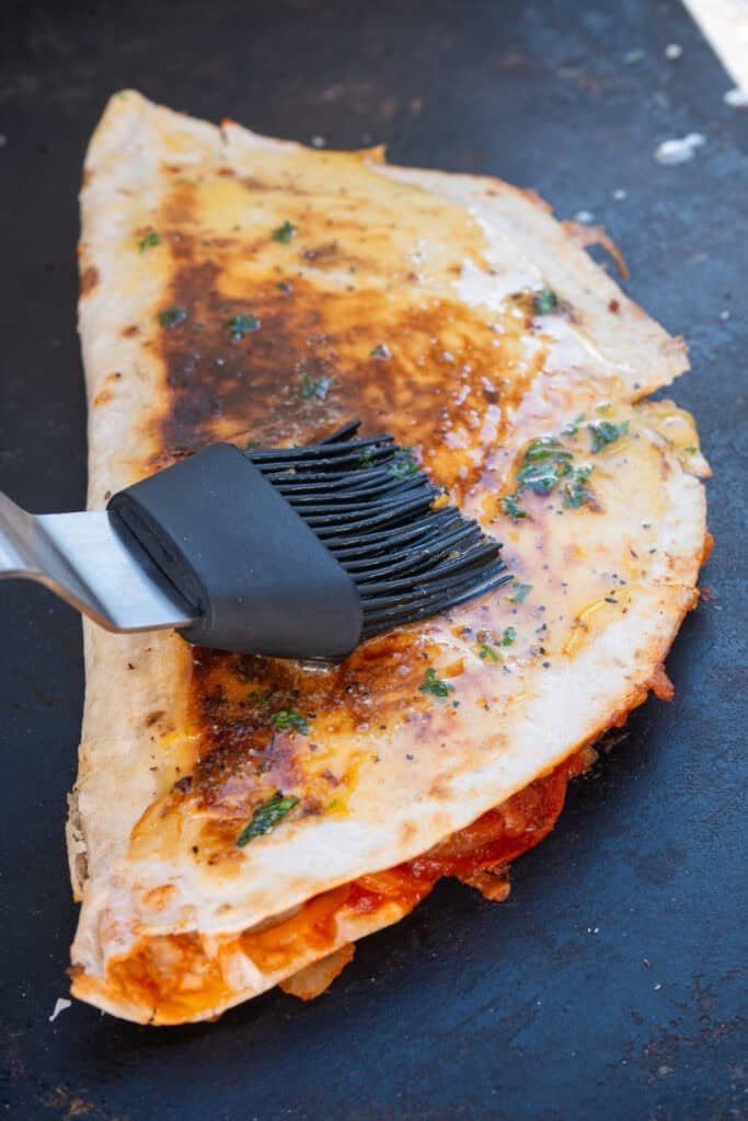 Pizza quesadillas being brushed with garlic herb butter.