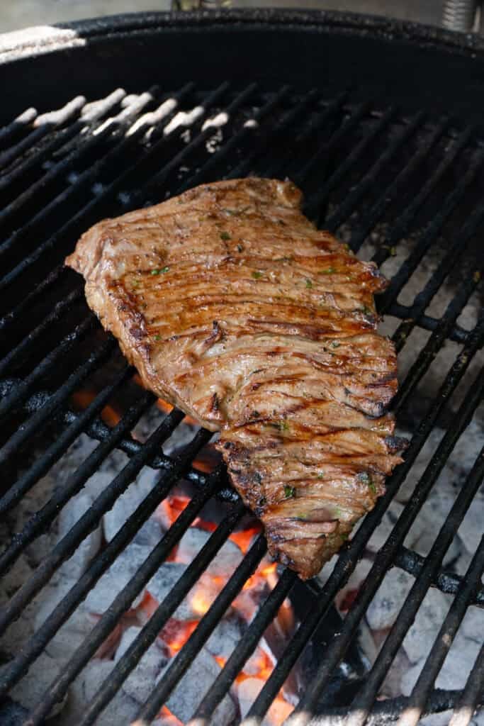 Skirt steak being grilled on a charcoal grill.