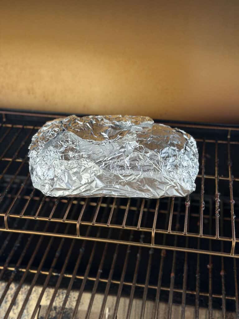pastrami wrapped in foil on the smoker.