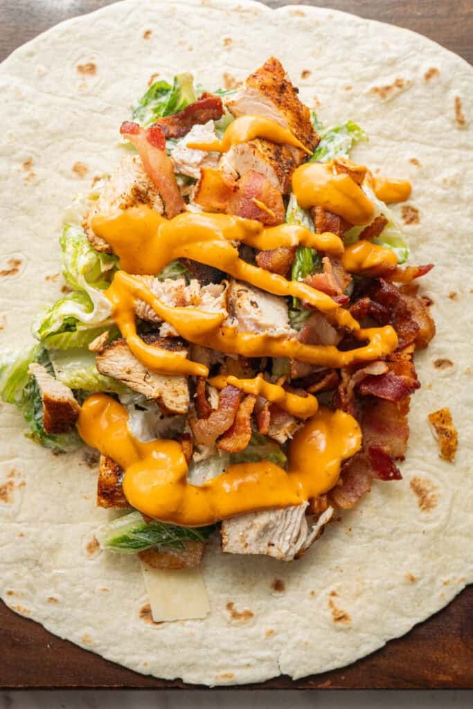 Grilled chicken caesar wrap ingredients on a tortilla.