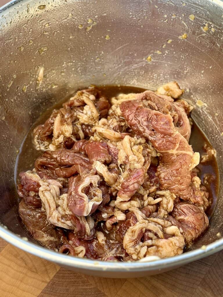 Shaved ribeye steak marinating in a bowl.