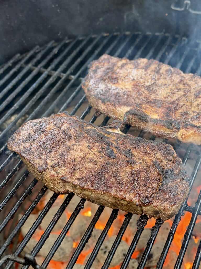 Ribeye steaks cooking on a grill.