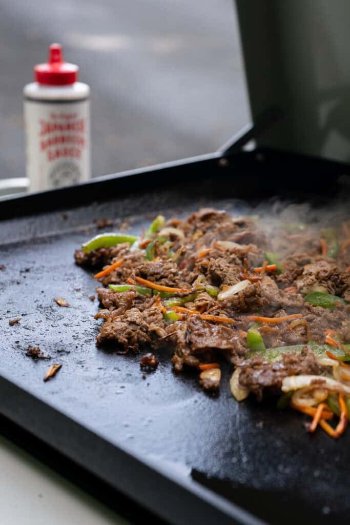Beef and vegetables cooking on griddle.