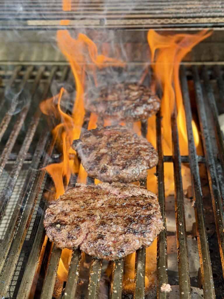 Burgers cooking with flame on grill.