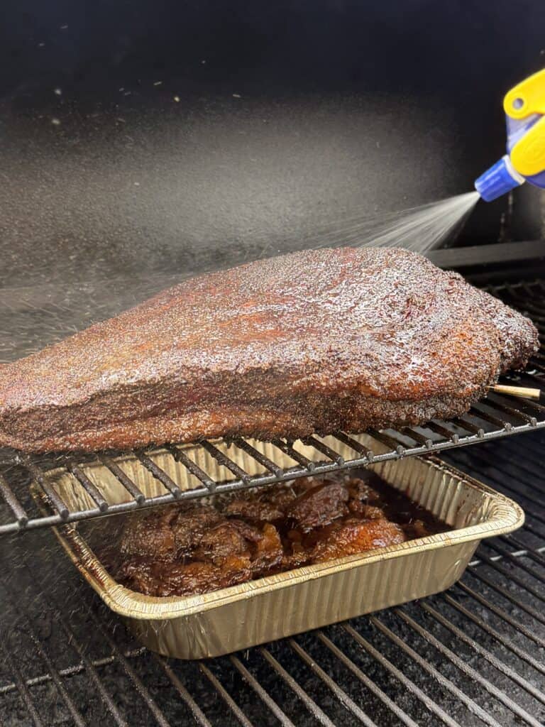 Spraying brisket meat on smoker.