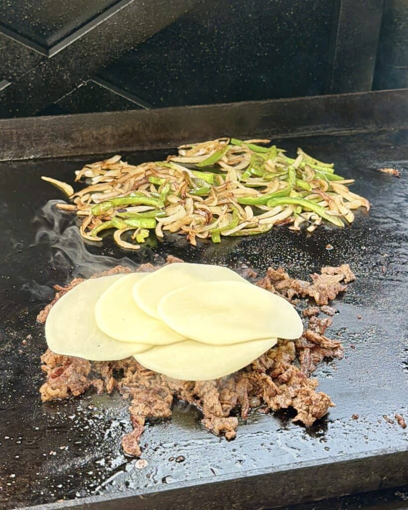 Cheesesteak with cheese on top cooking on griddle.