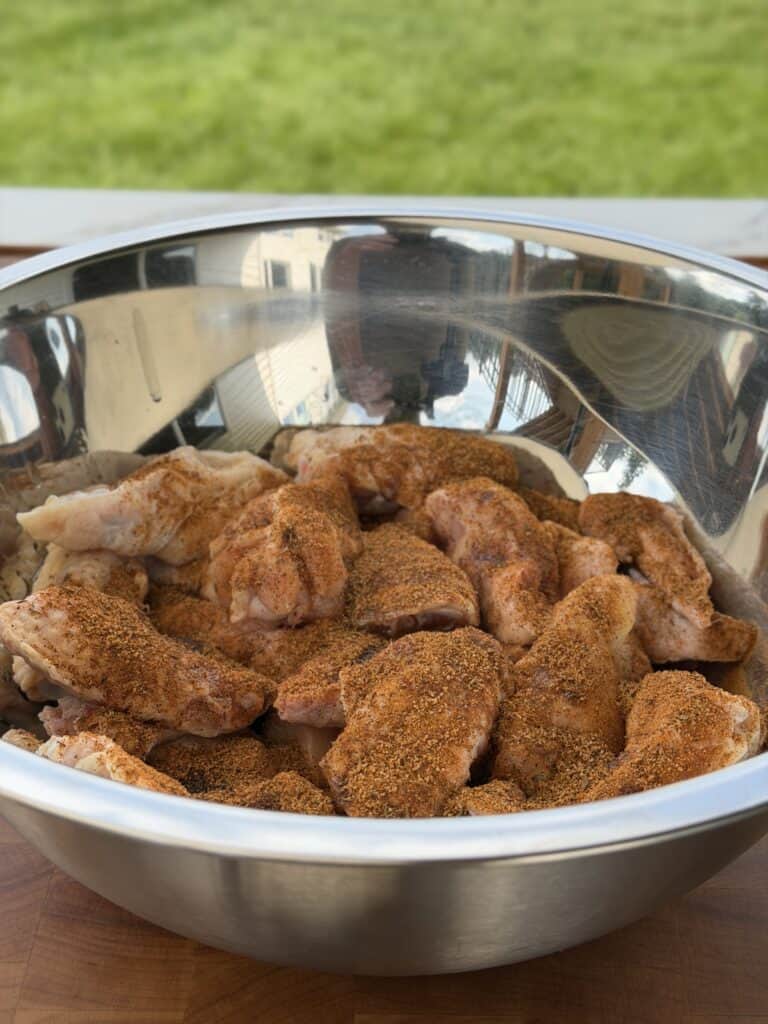 Seasoning chicken wings in metal bowl.