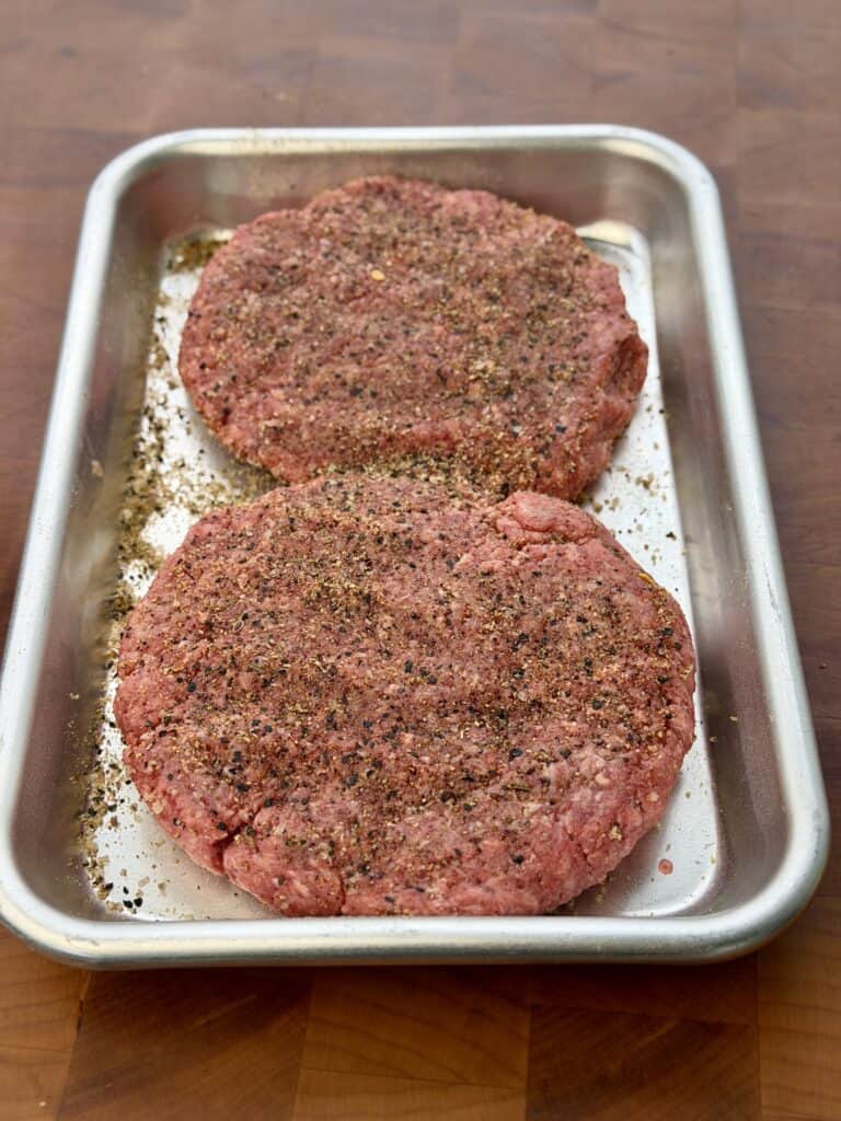 Seasoned burger in pan.