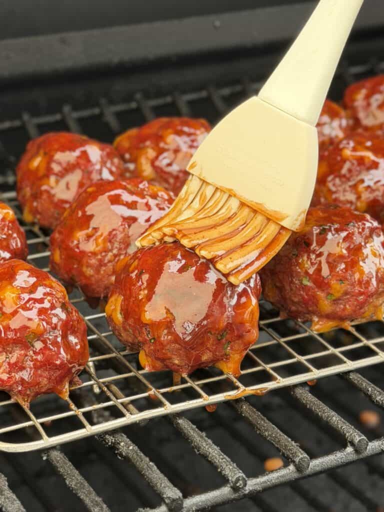 Brushing BBQ sauce on meatballs.